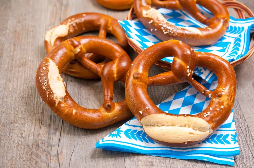 Ein Holztisch auf welchem blau-weiße Servierten und Brezen liegen.