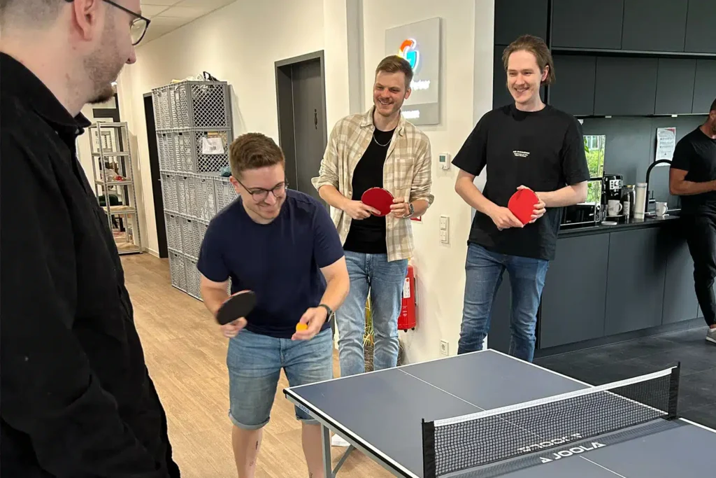 Vier junge Mitarbeiter spielen während ihrer Arbeitspause Tischtennis im Büro der Online Rebellion.