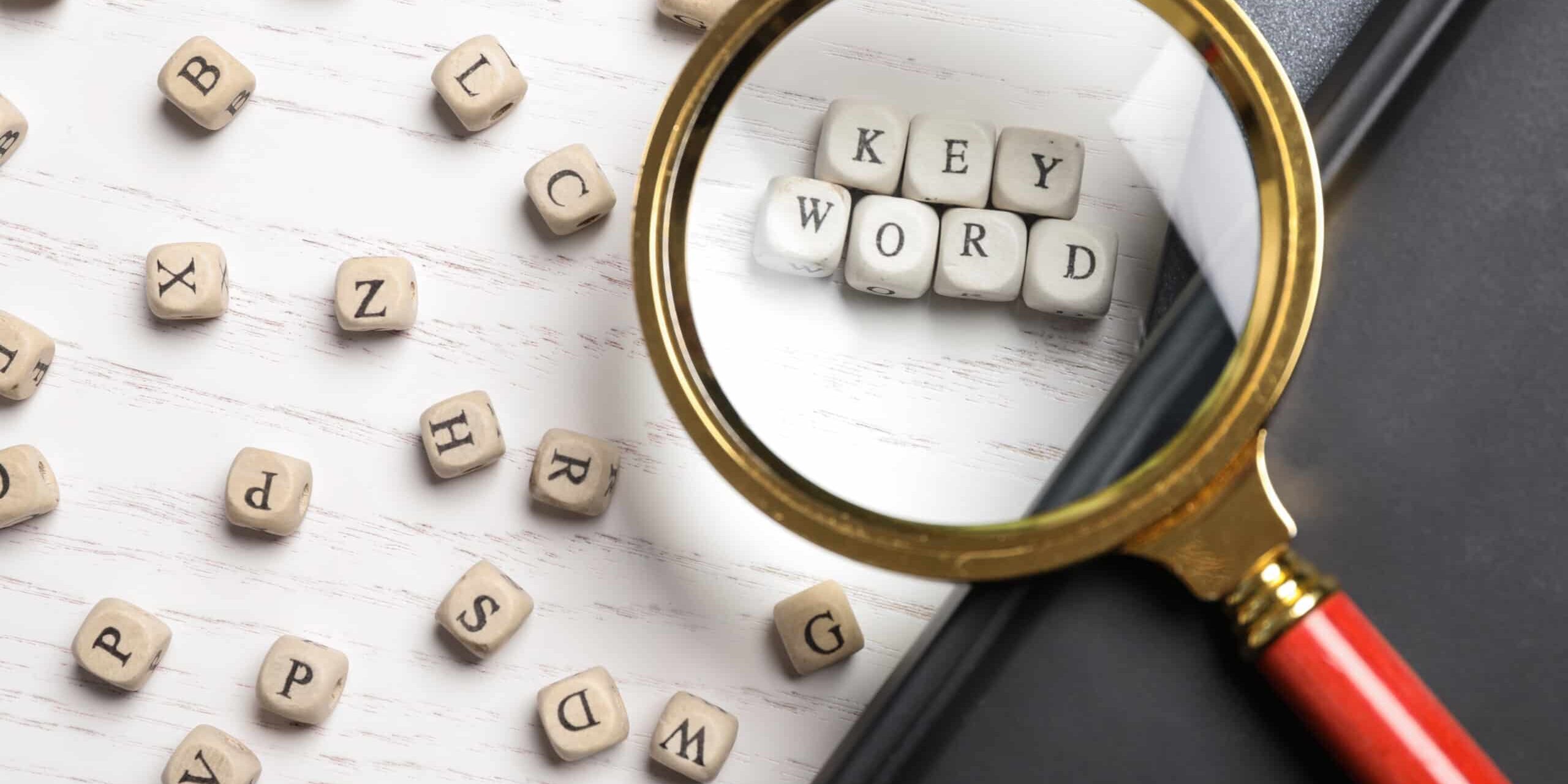 Looking at beads with word KEYWORD through magnifying glass at white wooden table, flat lay